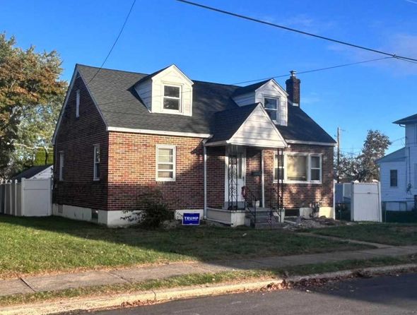 Brick house with a dark roof and two dormers under a blue sky, with a small yard.