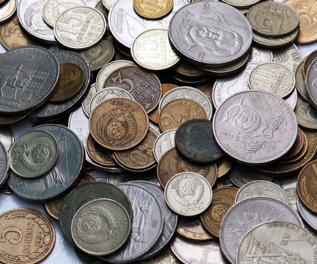 Pile of assorted old coins, mainly silver and bronze-toned, scattered on a surface. Some show details of figures and writing.