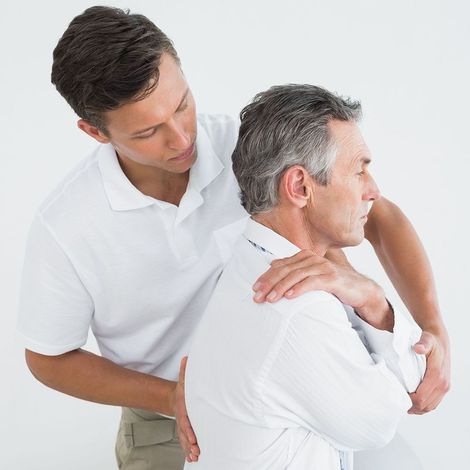 A man in a white shirt is helping another man with his back