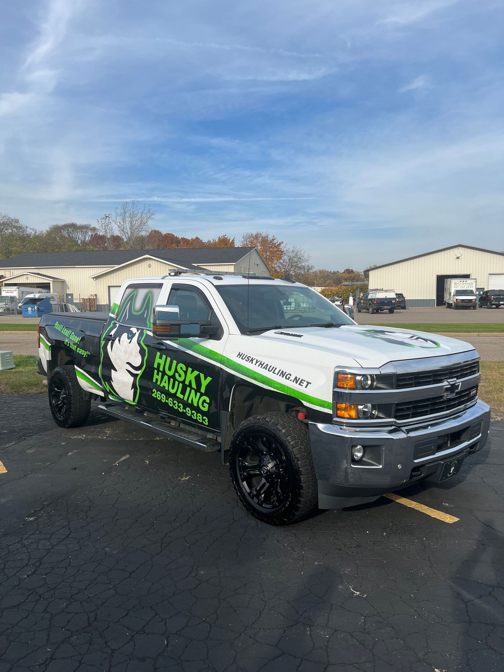White and black Husky Hauling truck with green logos parked on asphalt, cloudy sky backdrop.