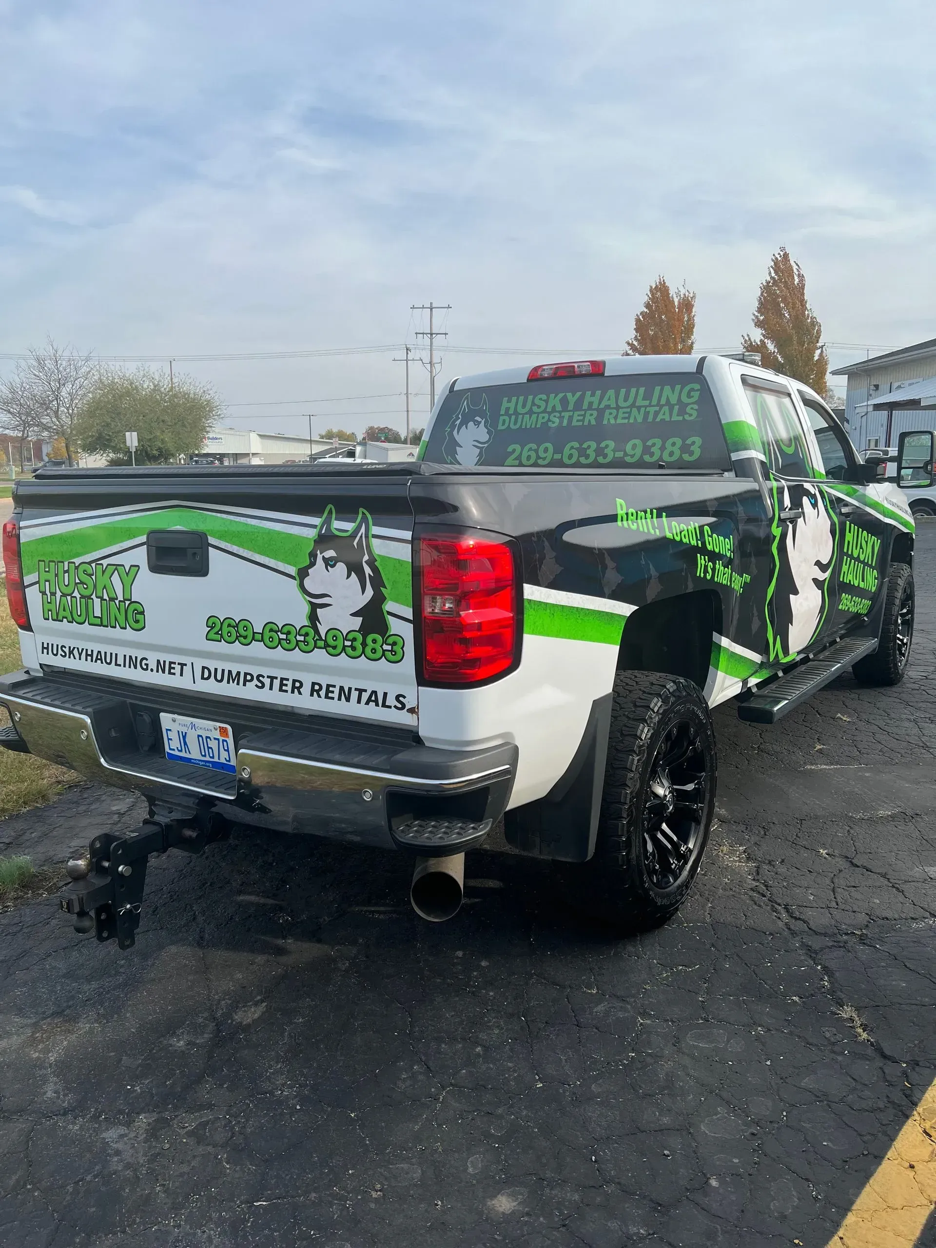 White truck with green and black business graphics, dog logo. Parked on asphalt.