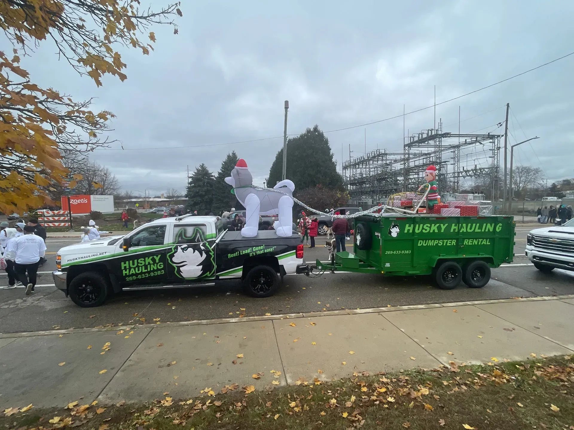 A decorated truck and trailer in a parade, with an inflatable husky and green trailer.