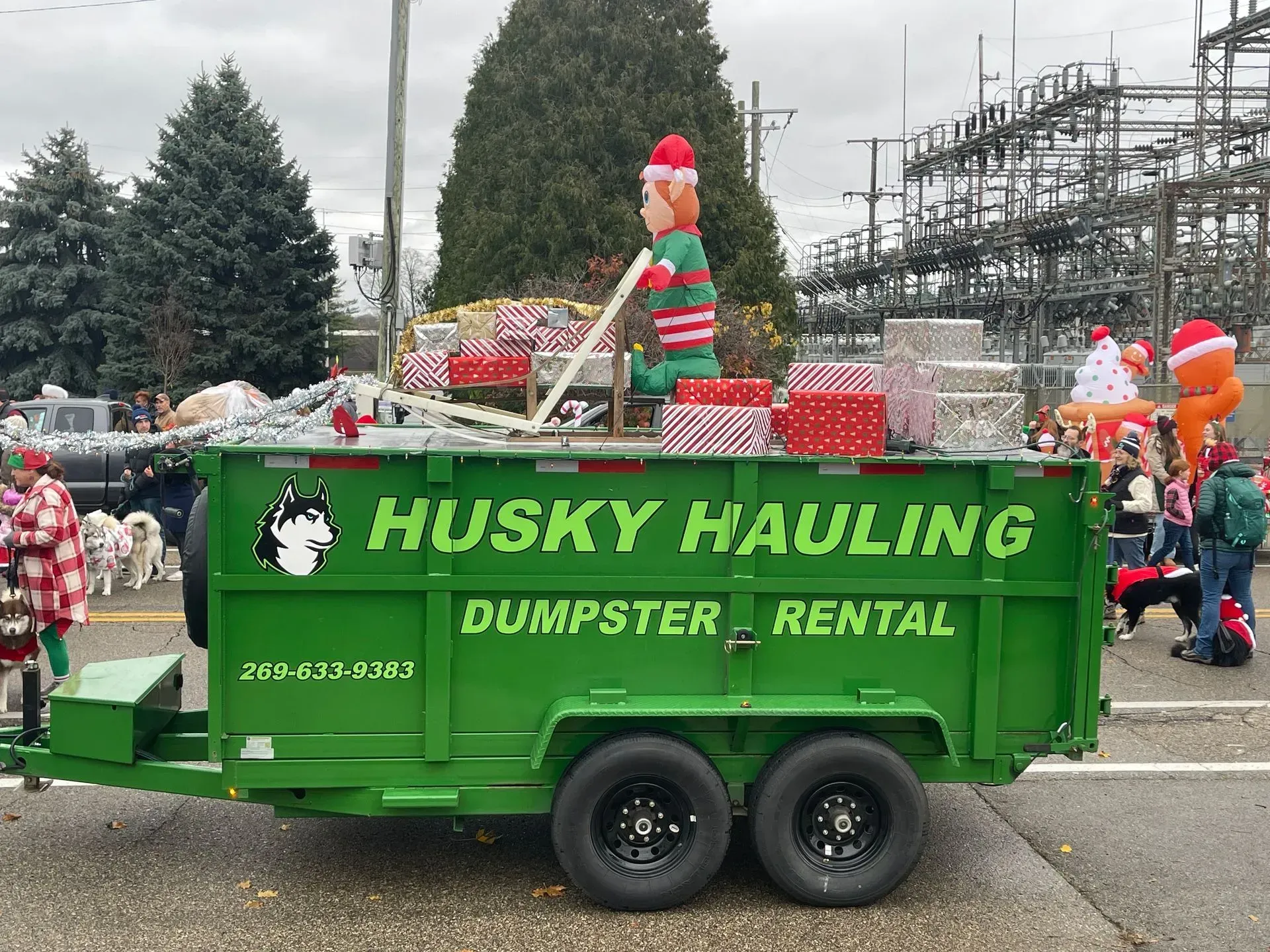 Husky Hauling dumpster trailer decorated for the holidays with elf figures and gifts, green and red.