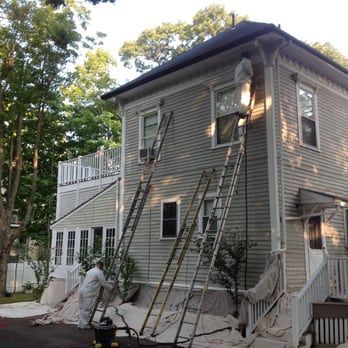 Two-story house with workers on ladders painting the gray exterior during renovation.