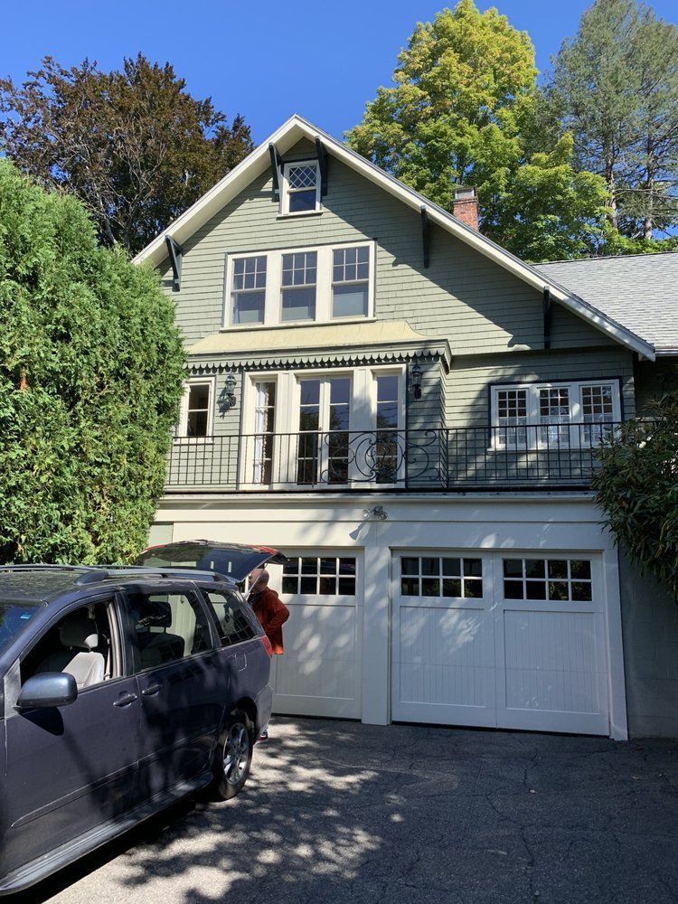 Two-story house with garage, balcony, and a parked black SUV in the driveway under a blue sky.