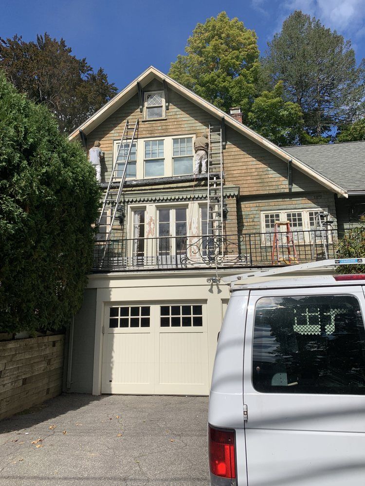 Two-story beige house with balcony and garage, partially blocked by a white van in front.