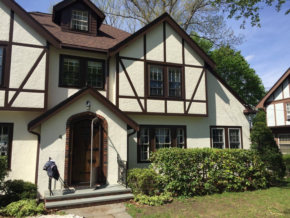 Tudor-style house exterior with white walls, dark trim, a front porch, and a person by the doorway