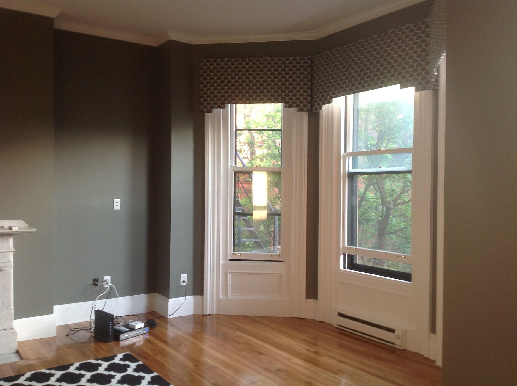 Empty living room with dark walls, bay windows, hardwood floors, and a white fireplace.