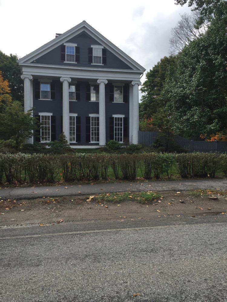 Large gray house with white columns and black shutters, seen from the street on an overcast day.