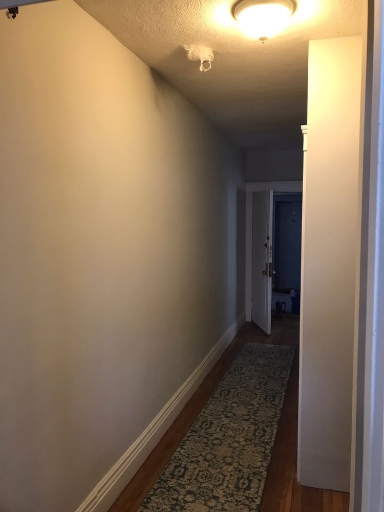 Narrow hallway with beige walls, patterned runner carpet, and ceiling lights leading to a doorway.