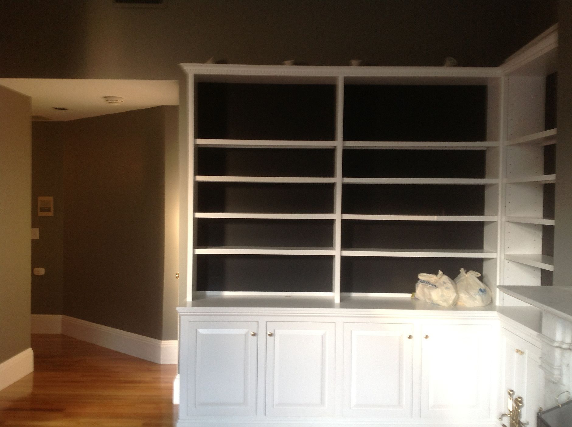 Built-in white shelving and cabinets in an empty room with brown walls and wood floors.