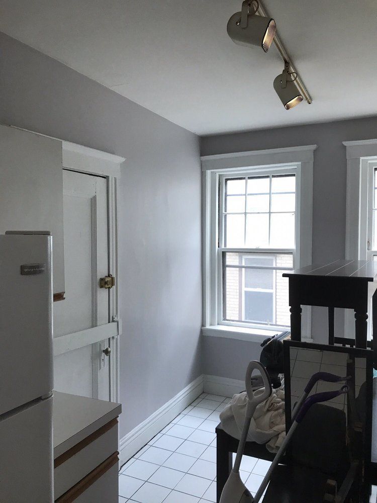 Small gray kitchen with white tile floor, window, refrigerator, and track lighting.