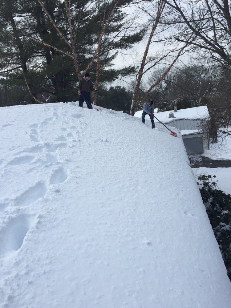 People standing on a huge snow-covered hill in a winter yard near trees and a house.