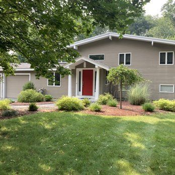 Suburban house with tan siding, red front door, and a landscaped green lawn