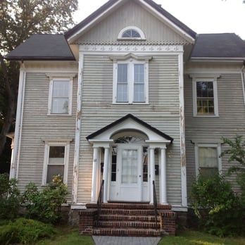 Old weathered two-story house with light siding, white trim, and a small front porch.