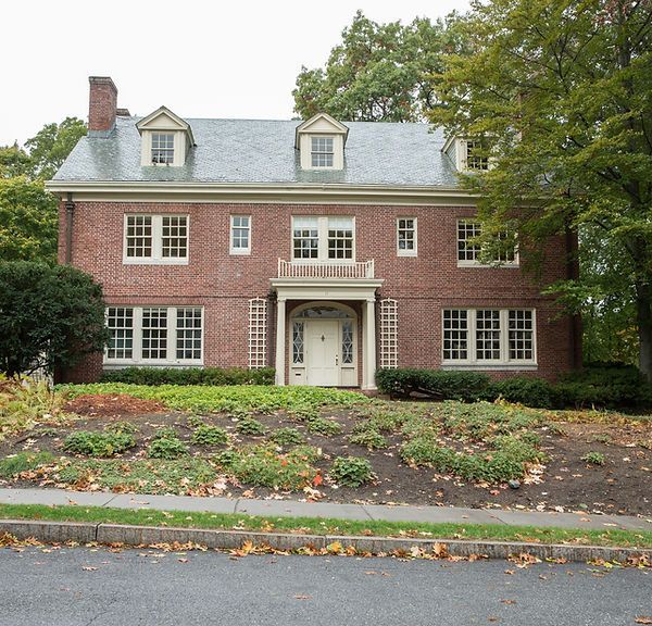 Brick two-story house with white trim, centered arched doorway, and autumn trees in front yard.