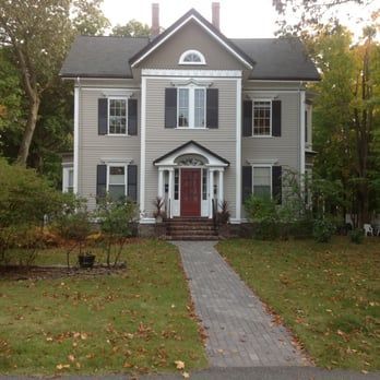 Gray two-story house with a red front door and a stone walkway through the lawn.