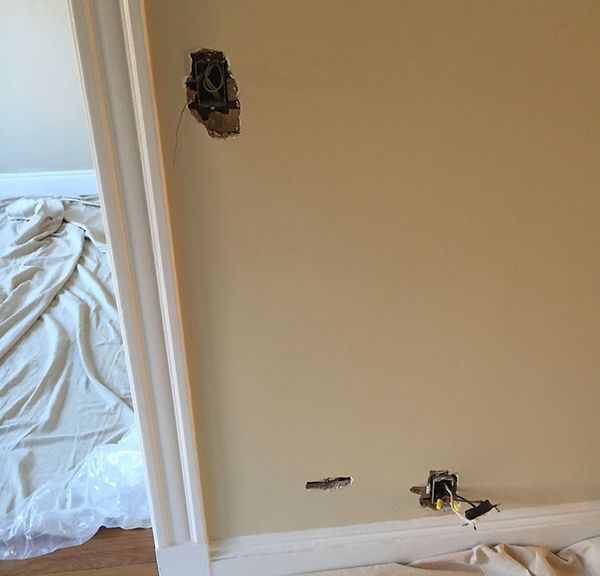 Damaged beige wall with holes and exposed wiring near a doorway in a room under repair.