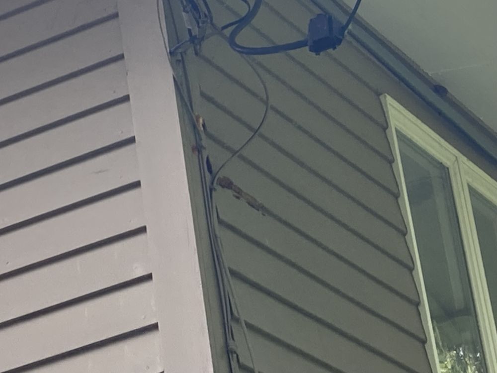 Side of a house with gray siding, white trim, and blue utility wires near a window.