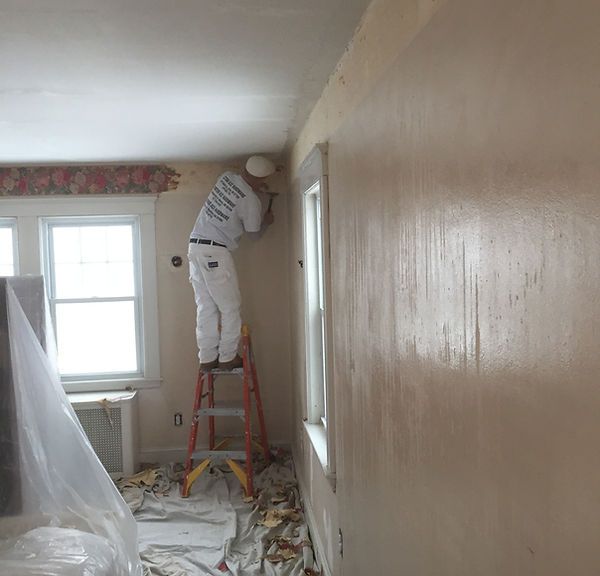 Painter on a red ladder working near the ceiling in a room under renovation, with drop cloths on the floor.