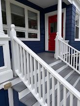 Front porch with white railing, gray steps, blue siding, and a red front door