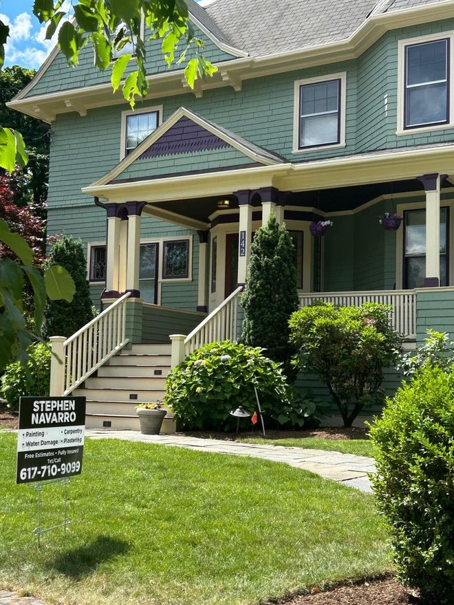 Green house with porch, stone walkway, and a real estate sign in the front yard.