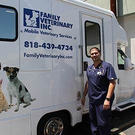 A person in blue medical scrubs stands next to a white Family Veterinary Inc. mobile clinic van.