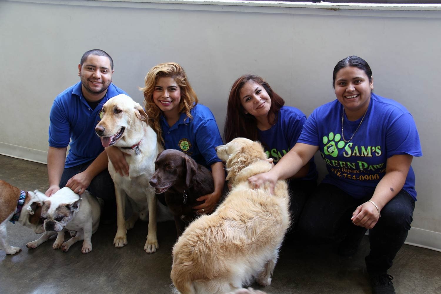Four people in matching blue shirts pose with five dogs in a bright, indoor facility.