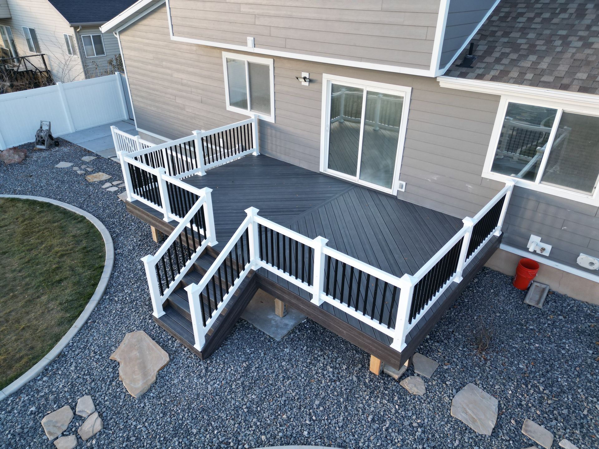 Backyard deck with white railings, gray siding, and sliding glass doors over gravel landscaping