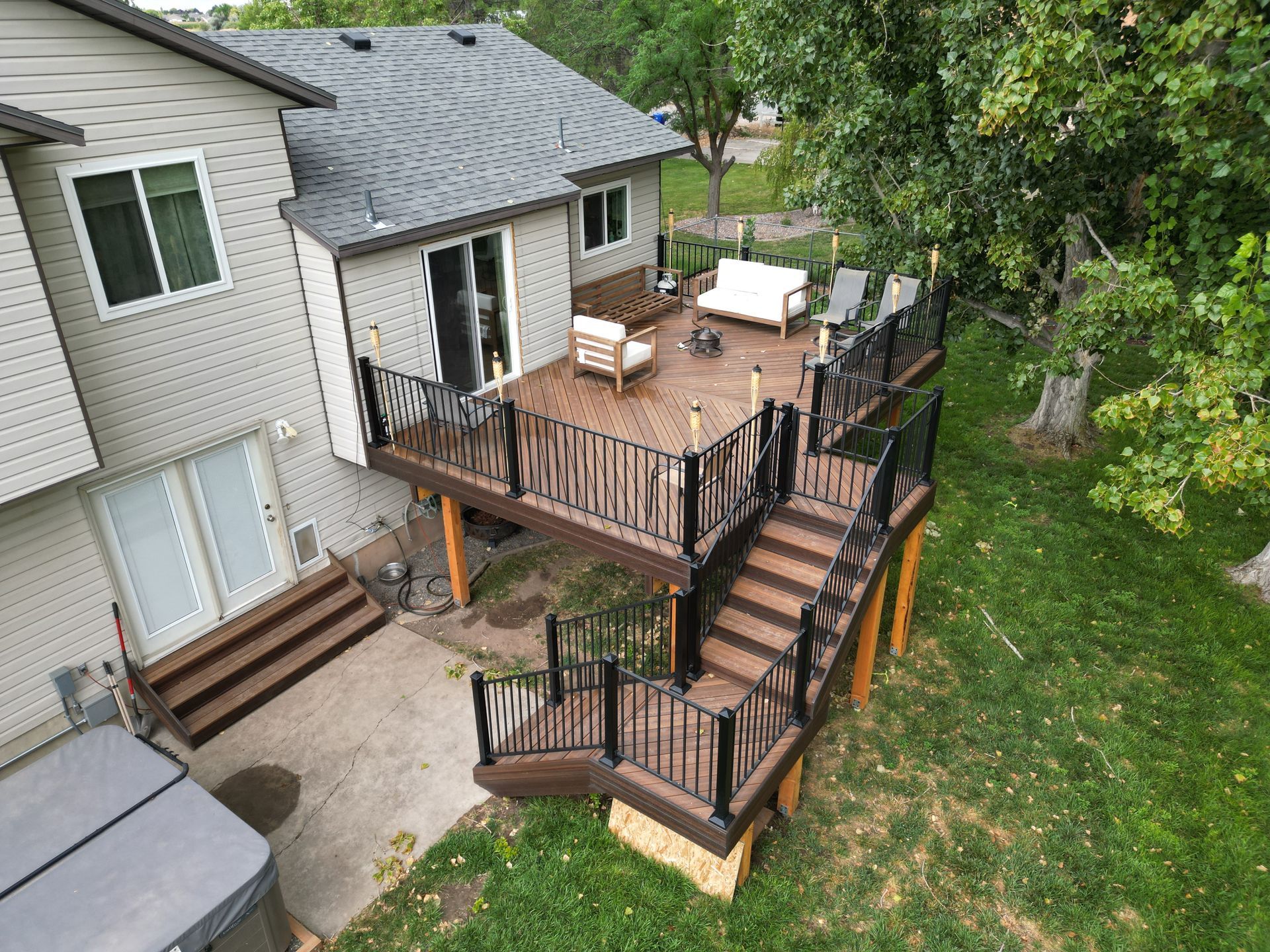 House deck and stairs with black railings, patio furniture, and a backyard lawn below.