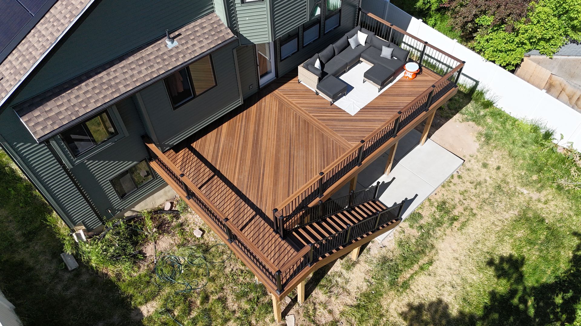 Aerial view of a house with a large wooden deck and patio furniture beside a grassy yard.