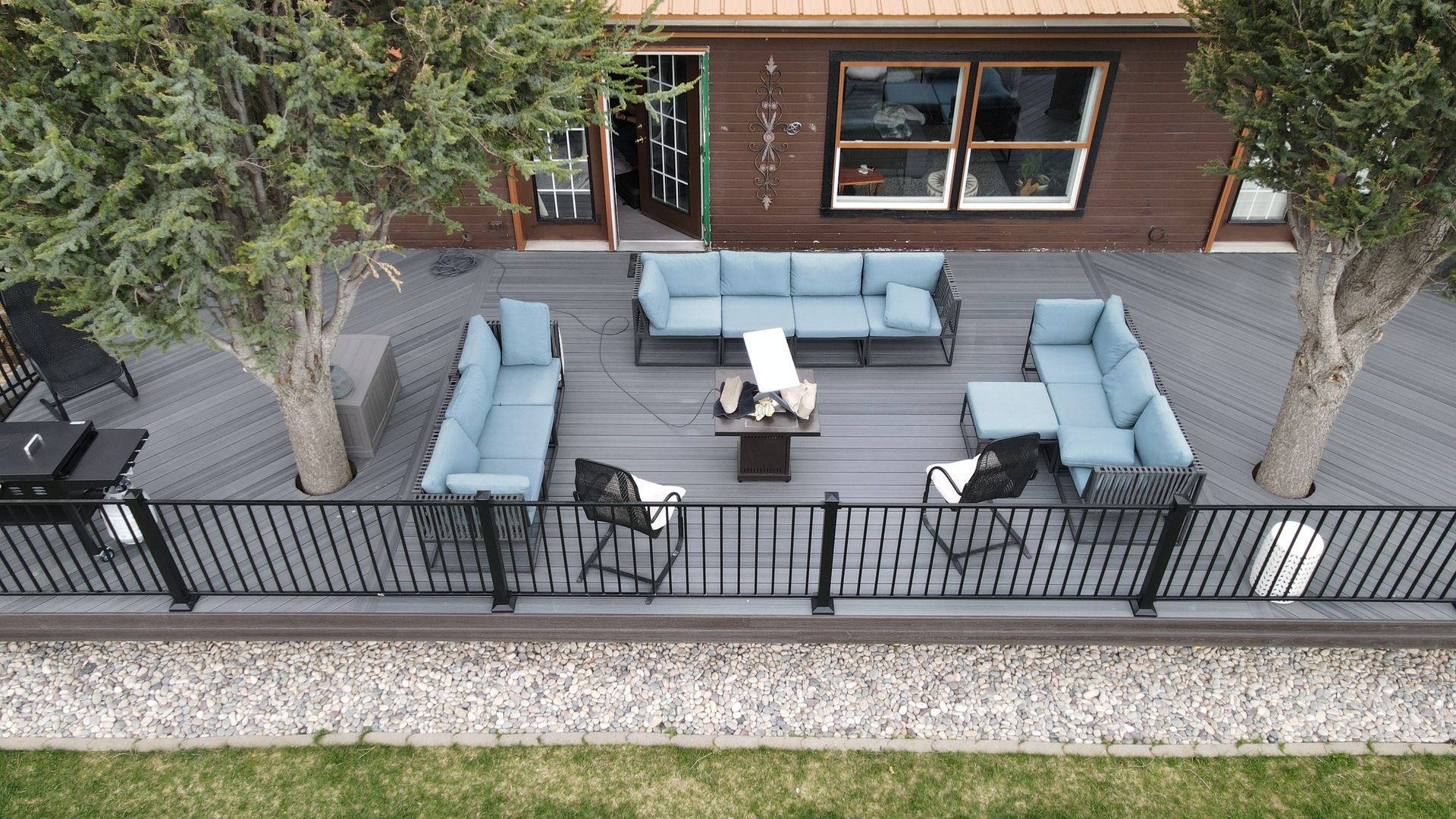 Overhead view of a fenced patio with blue outdoor seating and a coffee table beside a wooden building