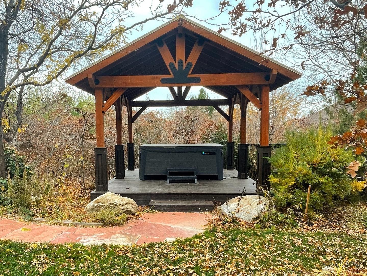 Wooden pavilion with a hot tub in an autumn garden, surrounded by trees and fallen leaves