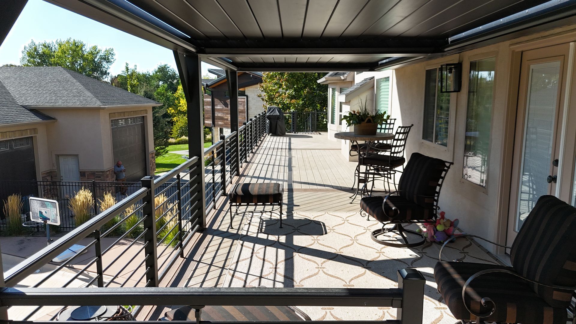 Covered front porch with black railing, chairs, and a small table overlooking a yard in daylight
