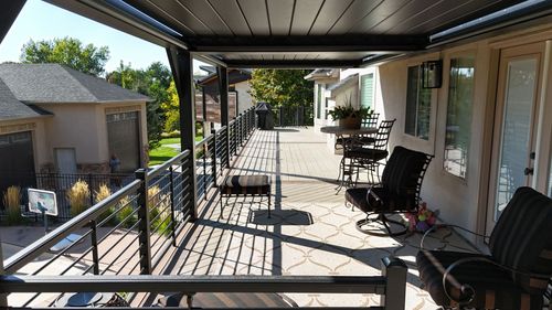 Covered front porch with black railing, chairs, and a small table overlooking a yard in daylight