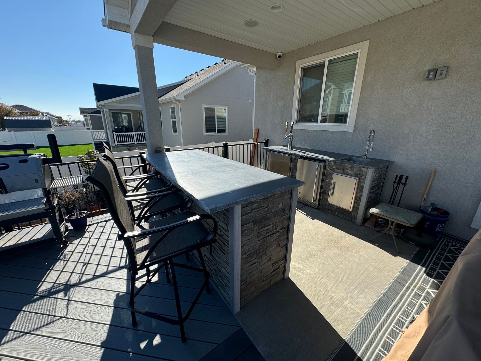 Covered patio with a black table and chairs beside a house, overlooking a grassy yard