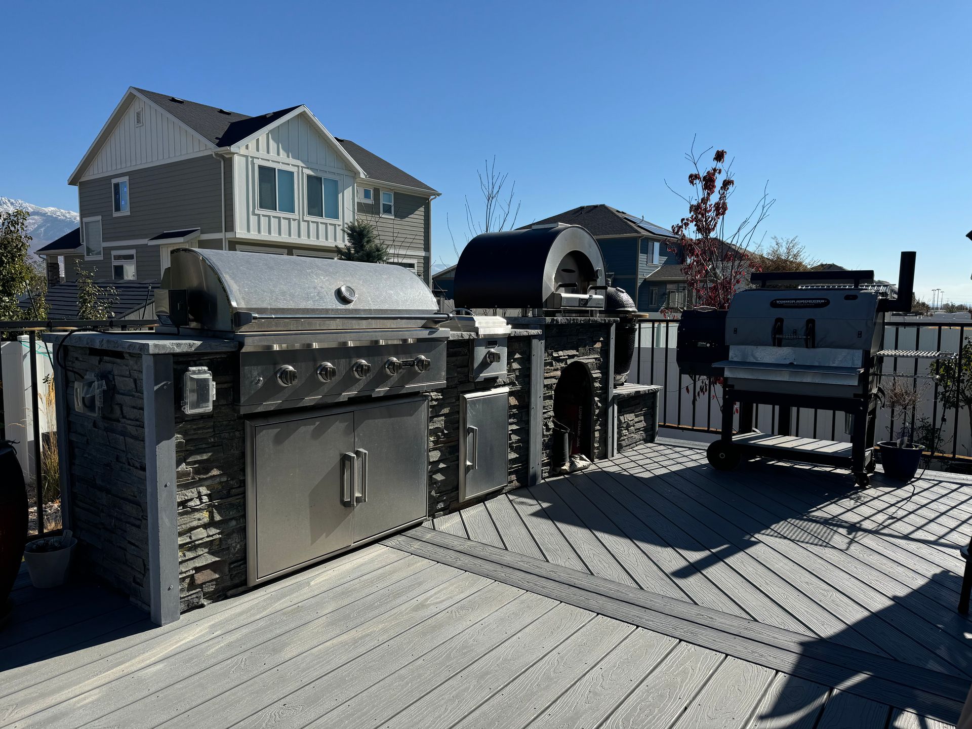 Outdoor kitchen and grill setup on a wooden deck beside a house on a clear day