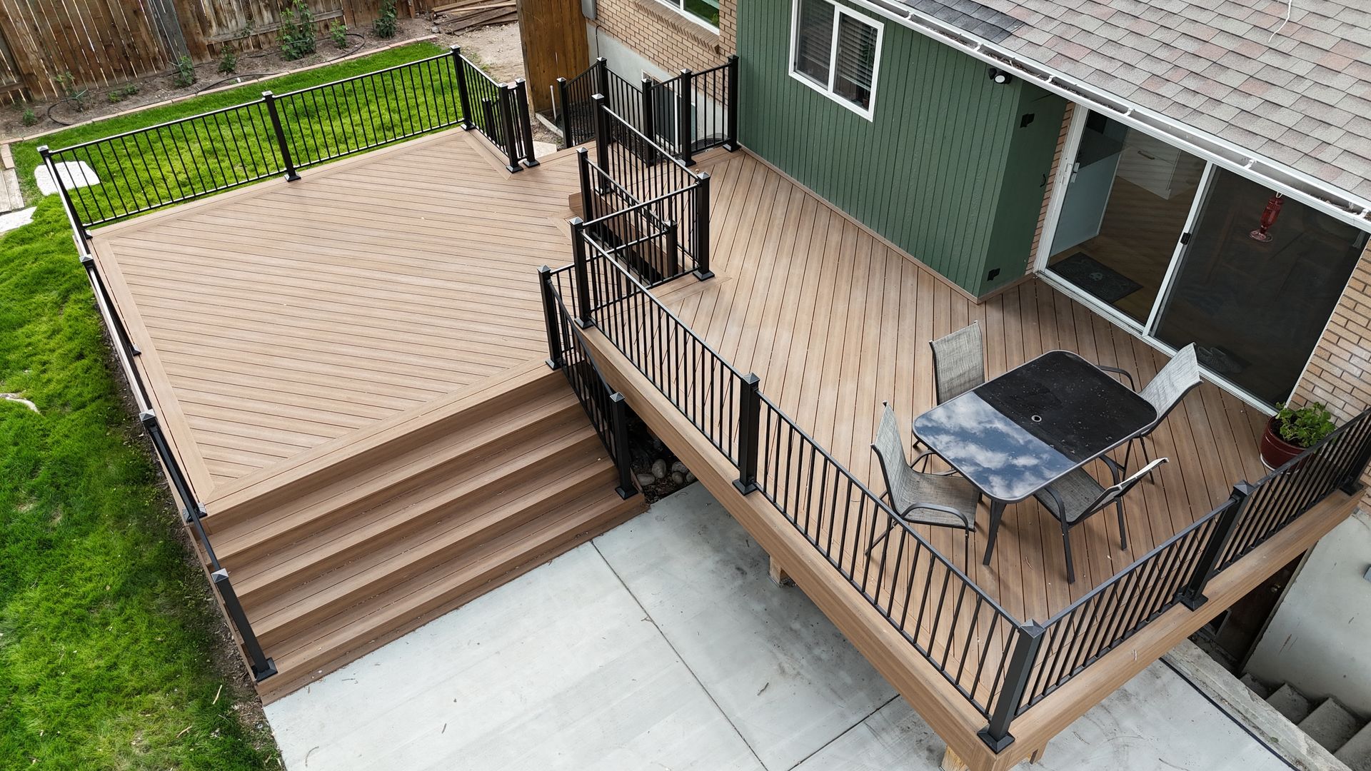 Raised wooden deck with stairs, black railing, grill, and patio table beside a house