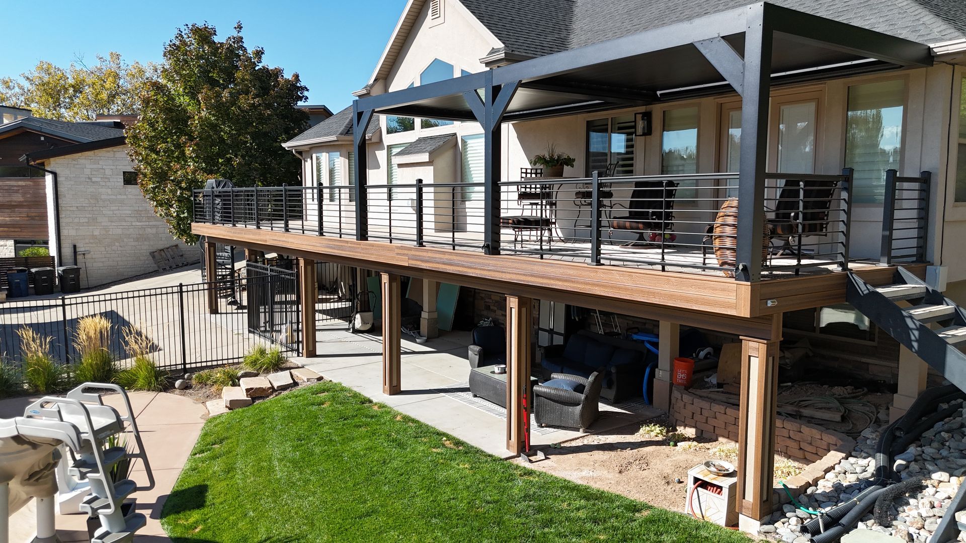 Backyard deck with wooden pergola, patio furniture, and green lawn beside a house