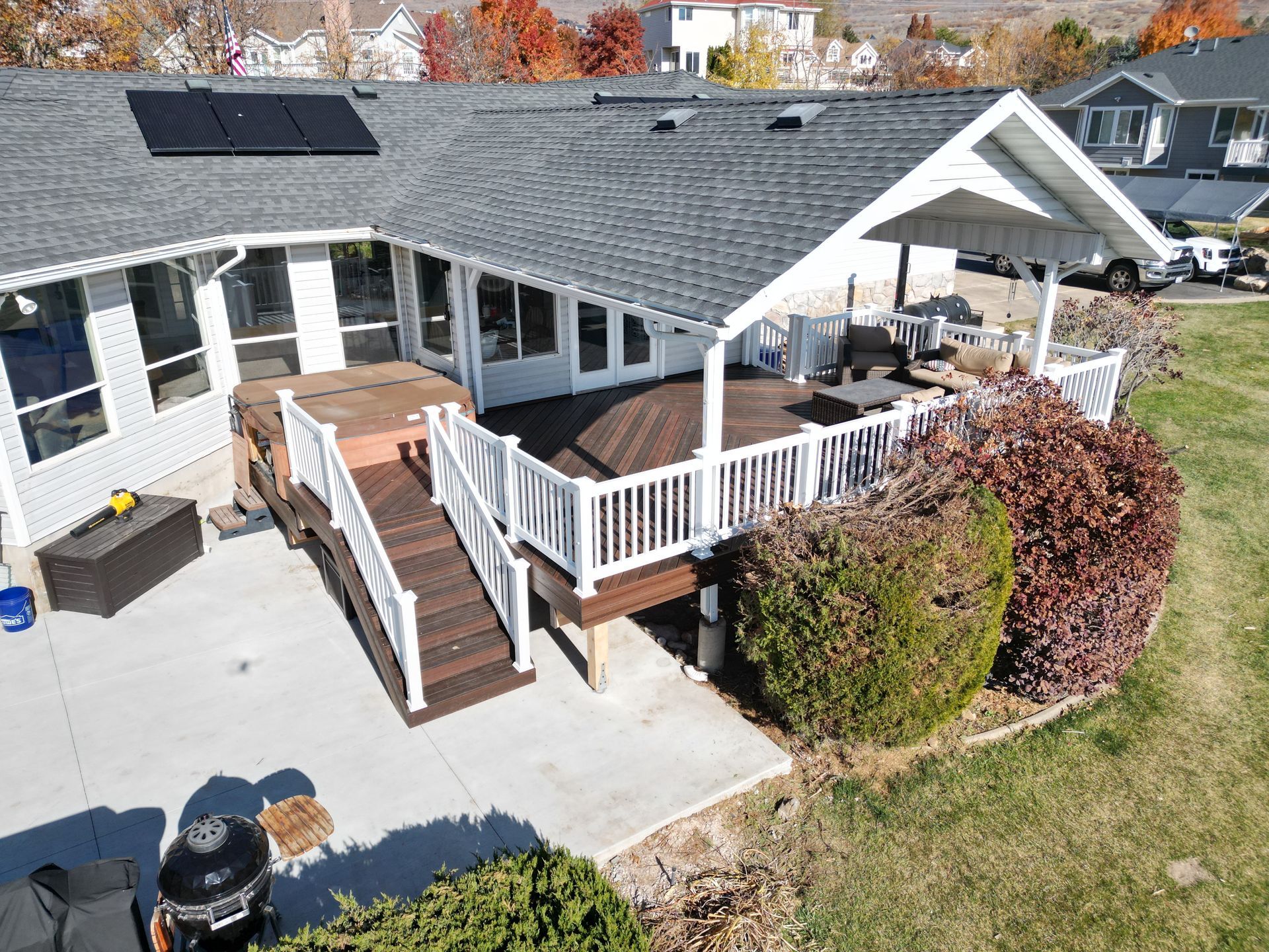 Backyard deck with white railings, gray house roof, patio furniture, and steps to a concrete patio