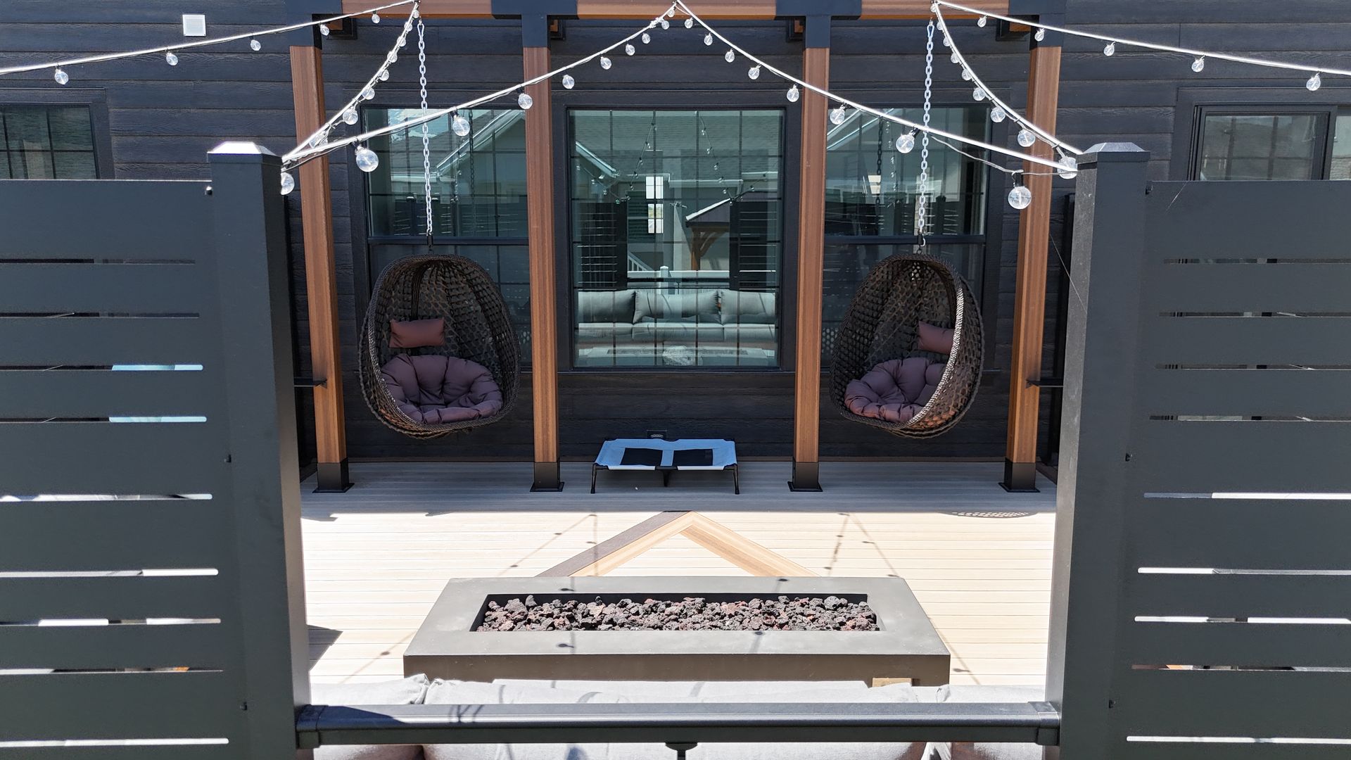 Patio with hanging wicker chairs, string lights, and a fire pit in front of a glass door