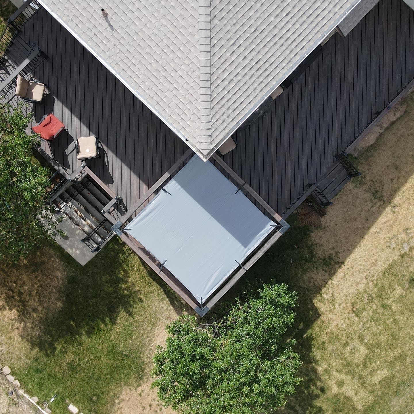 Aerial view of a house corner with a light gray roof, deck, and grassy yard with trees.