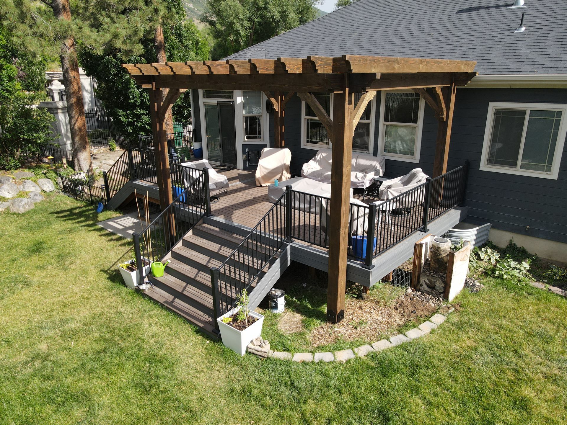 Backyard deck with pergola, stairs, and outdoor seating beside a gray house.