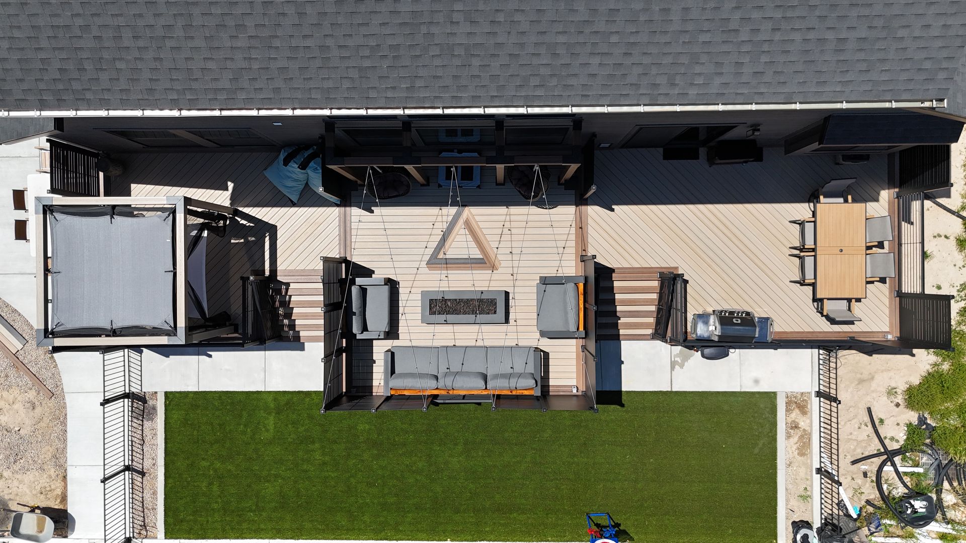 Top-down view of a backyard patio with outdoor seating, a pergola, and a green lawn beside a house.