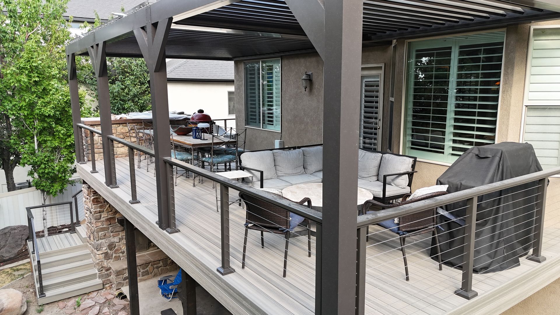 Covered patio with gray sofa, grill, and dining table on a wooden deck beside the house.