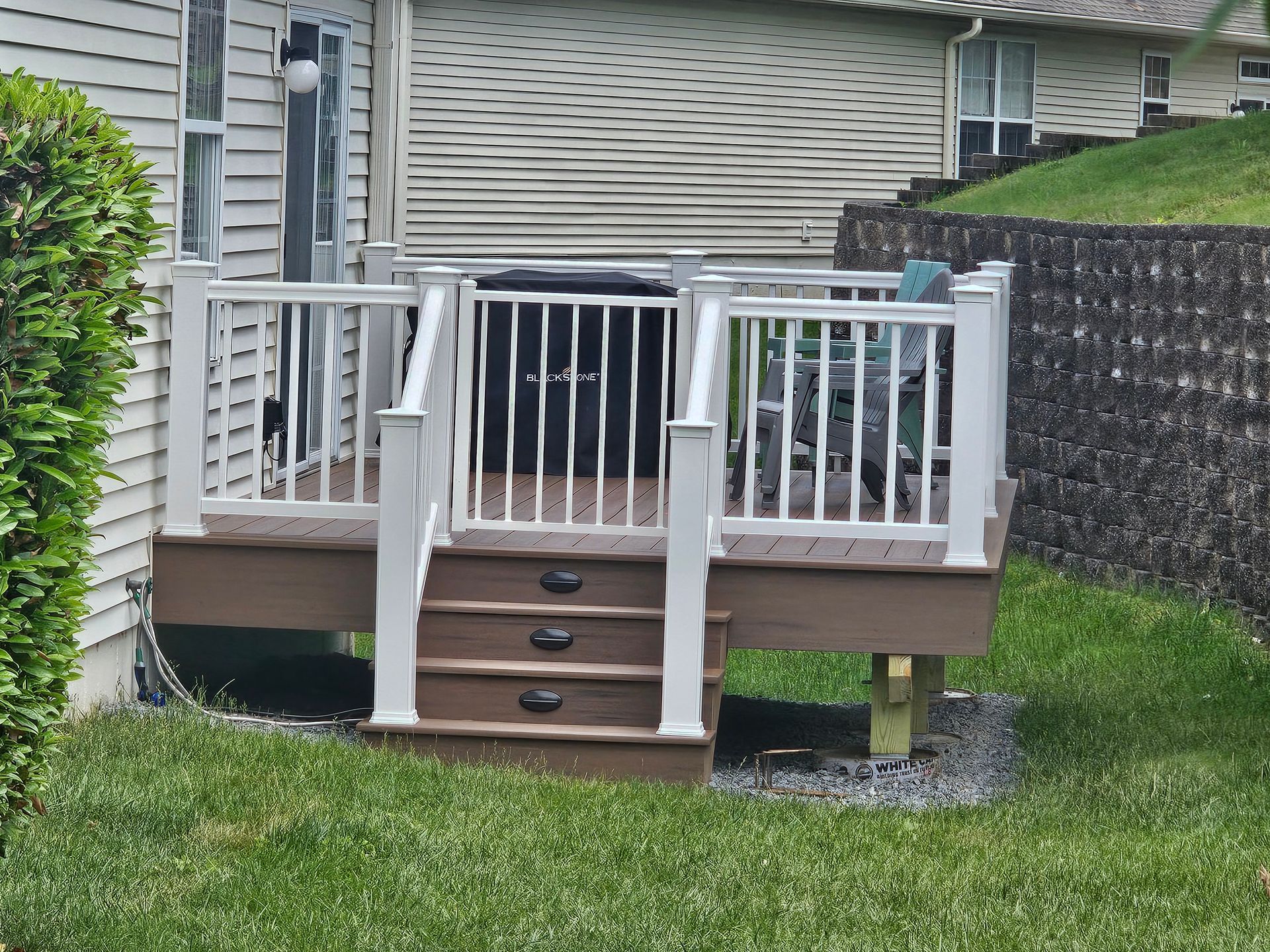 Backyard deck with white railings, black chair, and central steps leading to a grassy yard