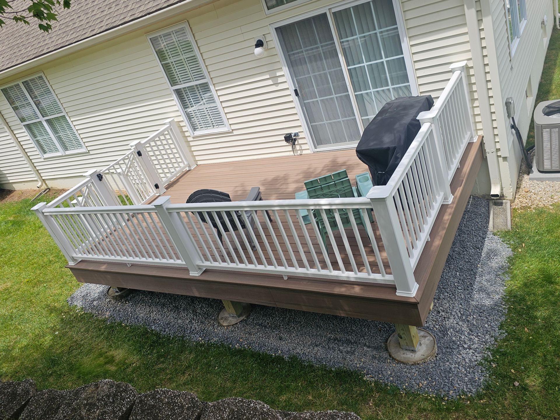 Small backyard deck with white railings, black grill, and outdoor furniture beside a house