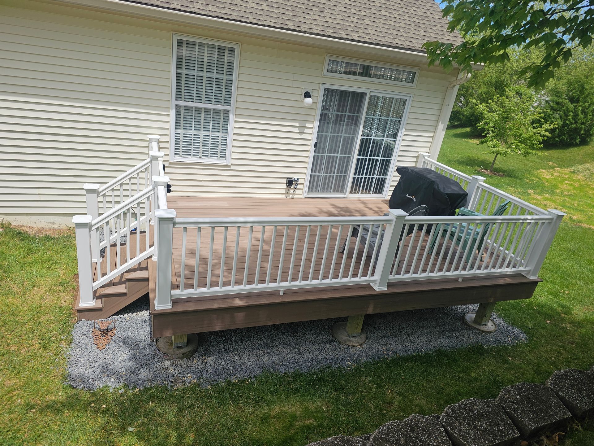 Raised wooden deck with white railings and stairs attached to a beige house, beside a grassy yard.