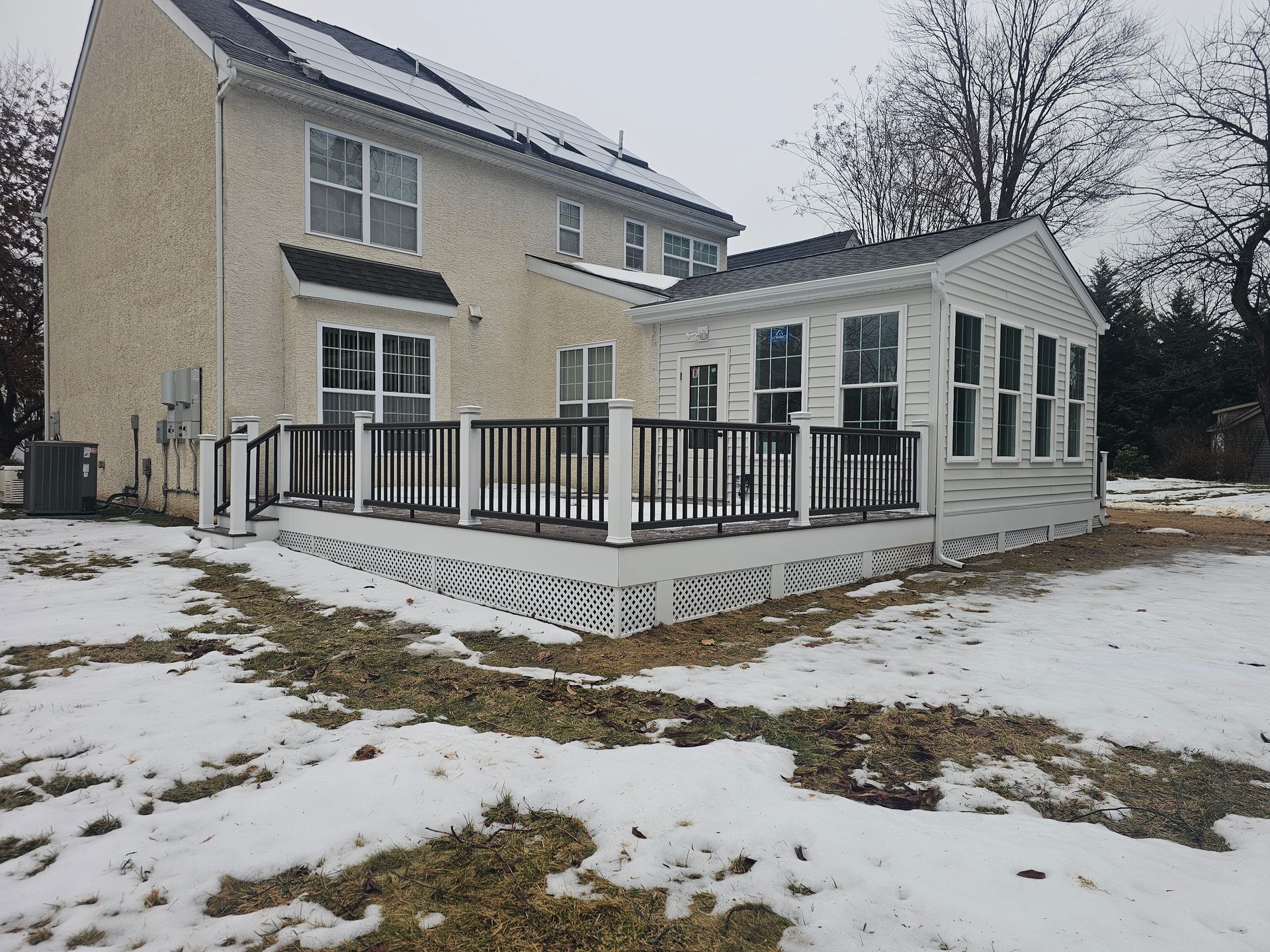 Snow-dusted backyard deck and sunroom attached to a beige two-story house