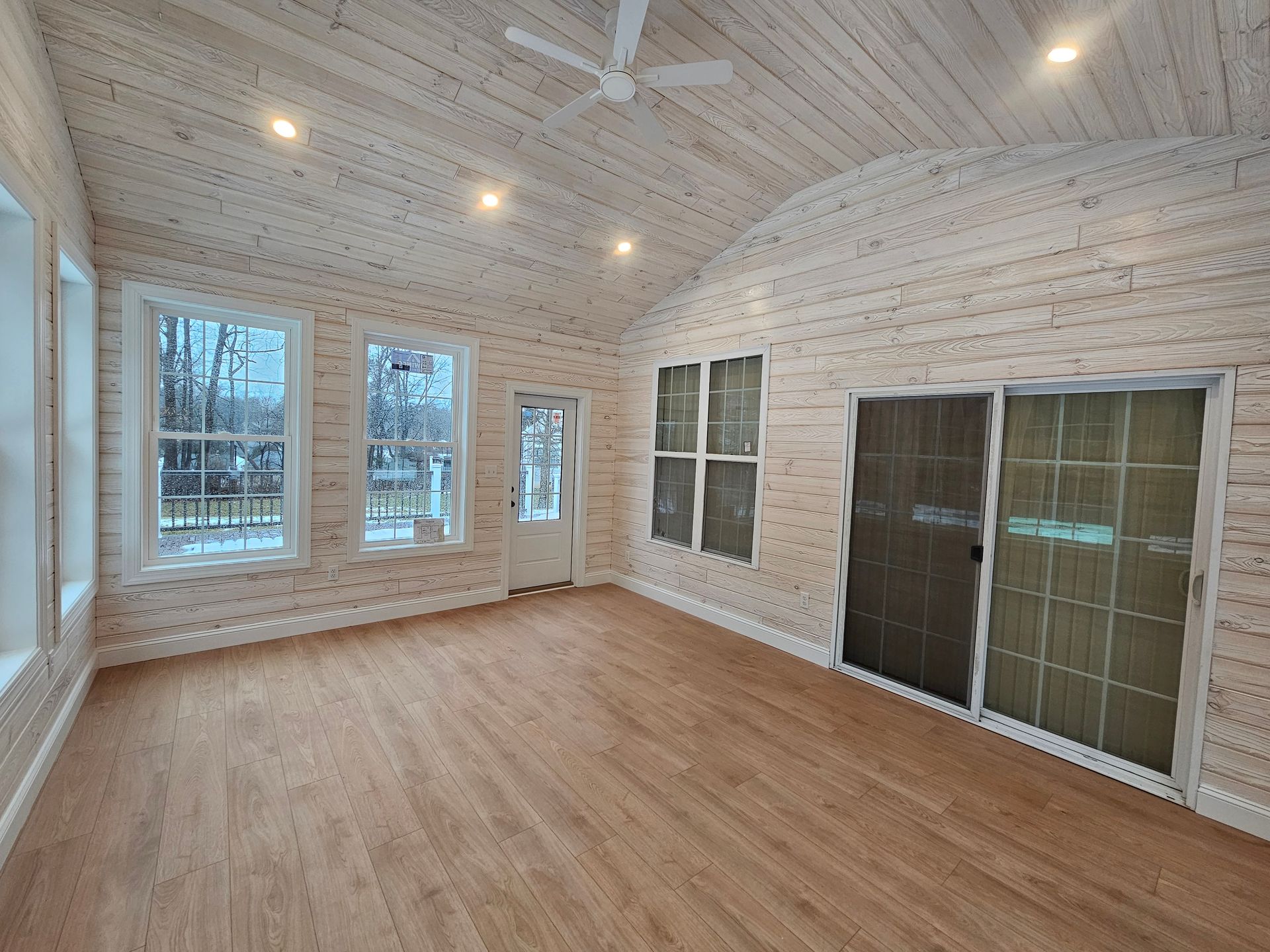 Empty sunroom with white wood ceiling, large windows, and light wood floors
